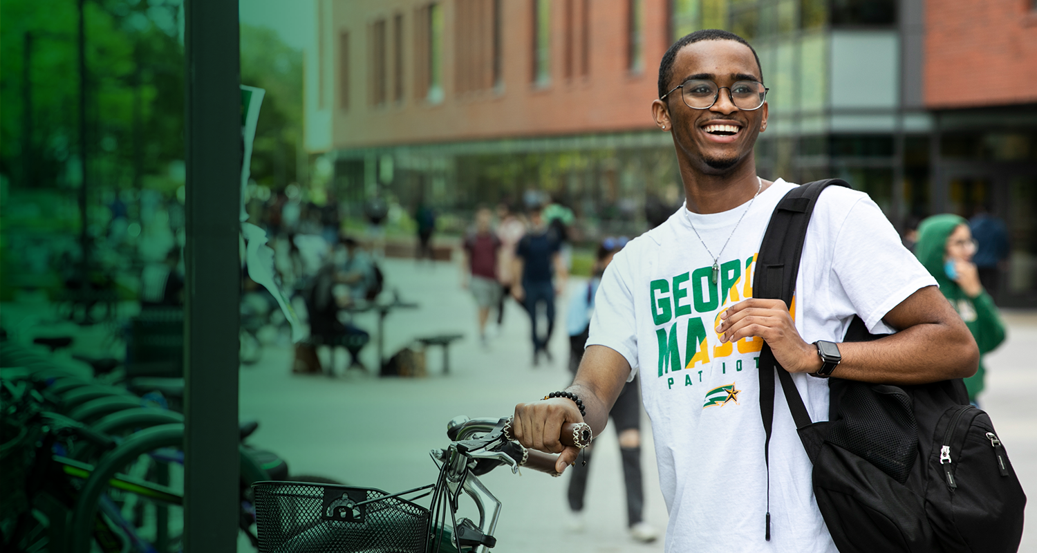 A Ƶ student stands next to a bike rack in Wilkins Plaza on the Fairfax Campus and smiles.